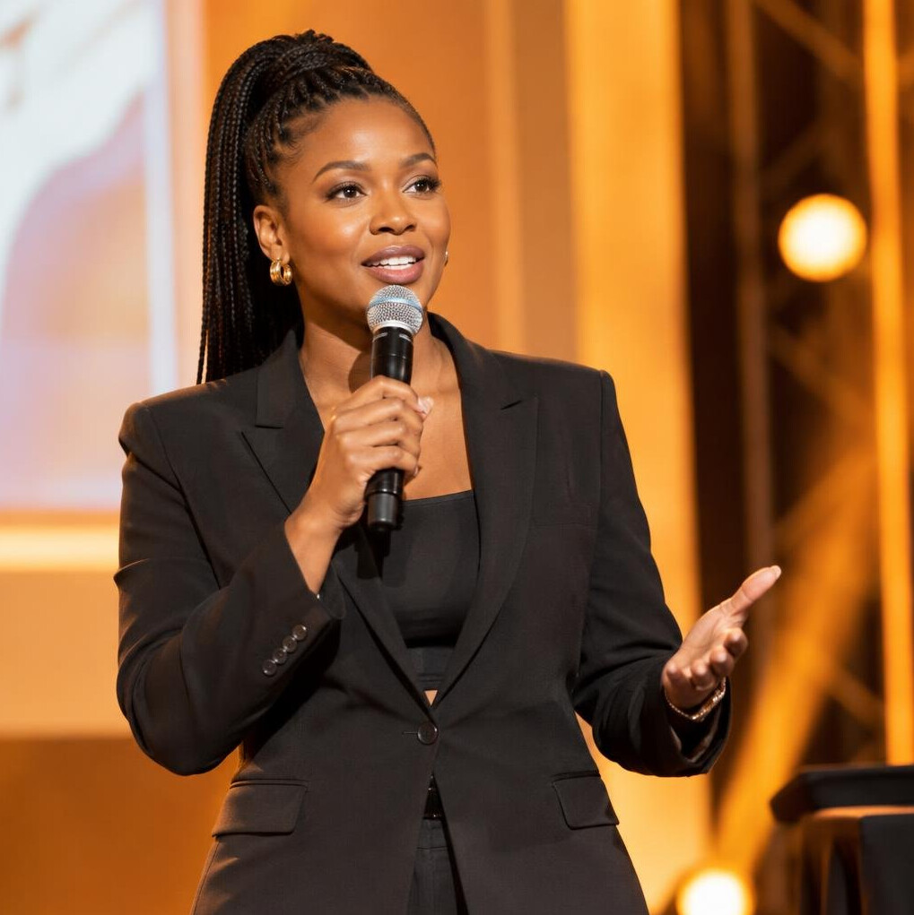 Female event host speaking into a microphone on a lit stage